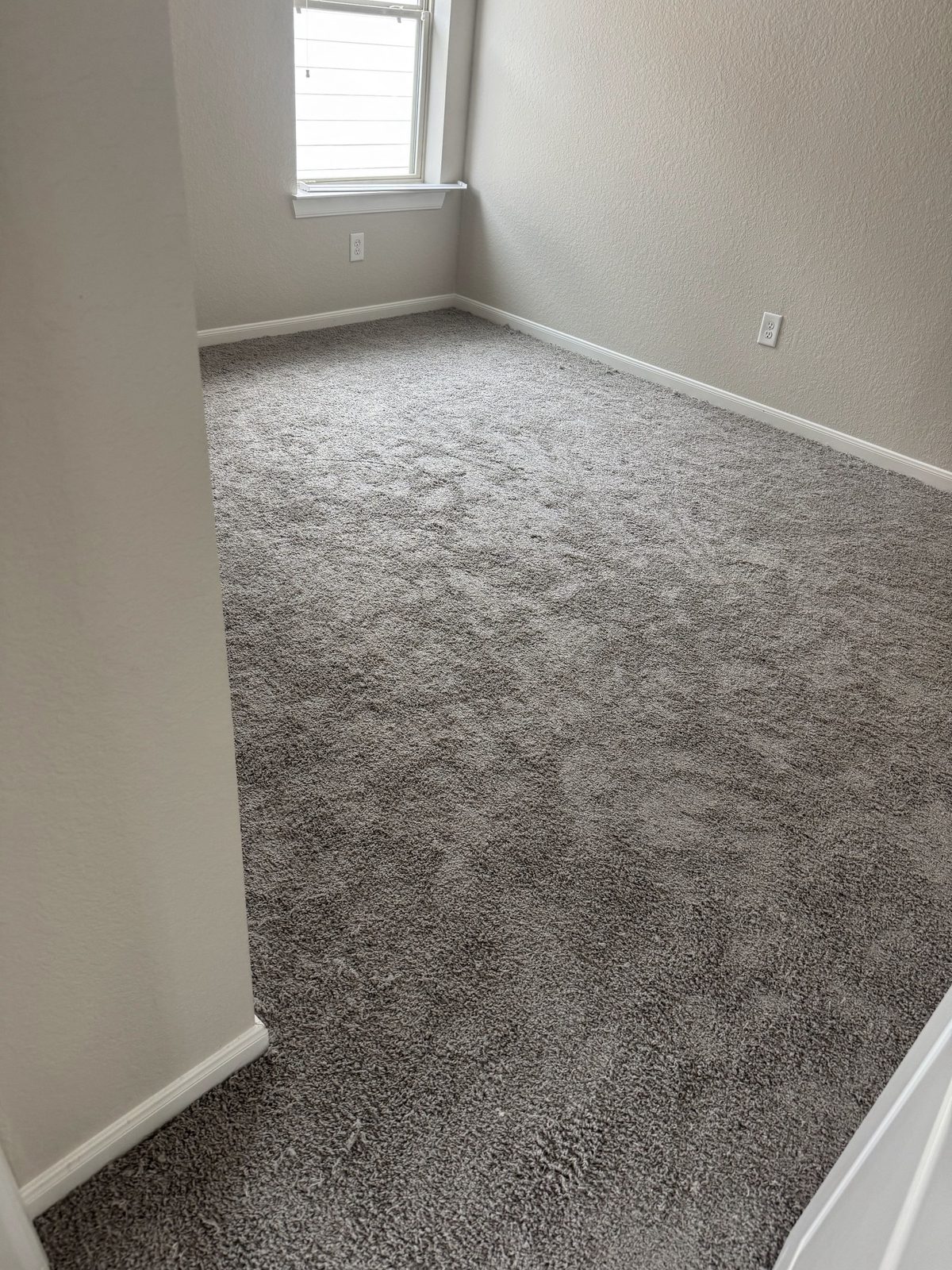 Gray plush carpet installed wall to wall in a bright bedroom