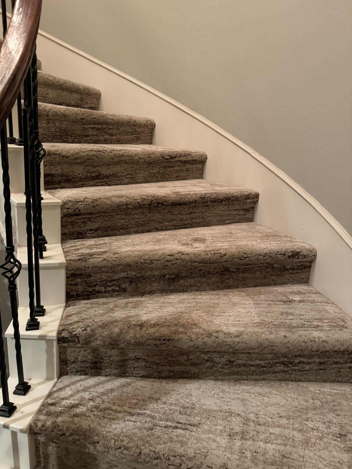 Carpeted staircase with black iron balusters and a wood handrail