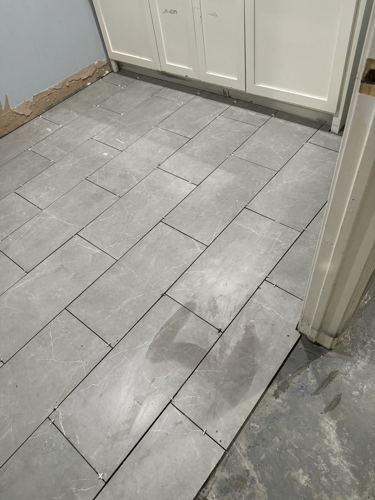 Gray ceramic floor tile mid-install with spacers still set in the joints
