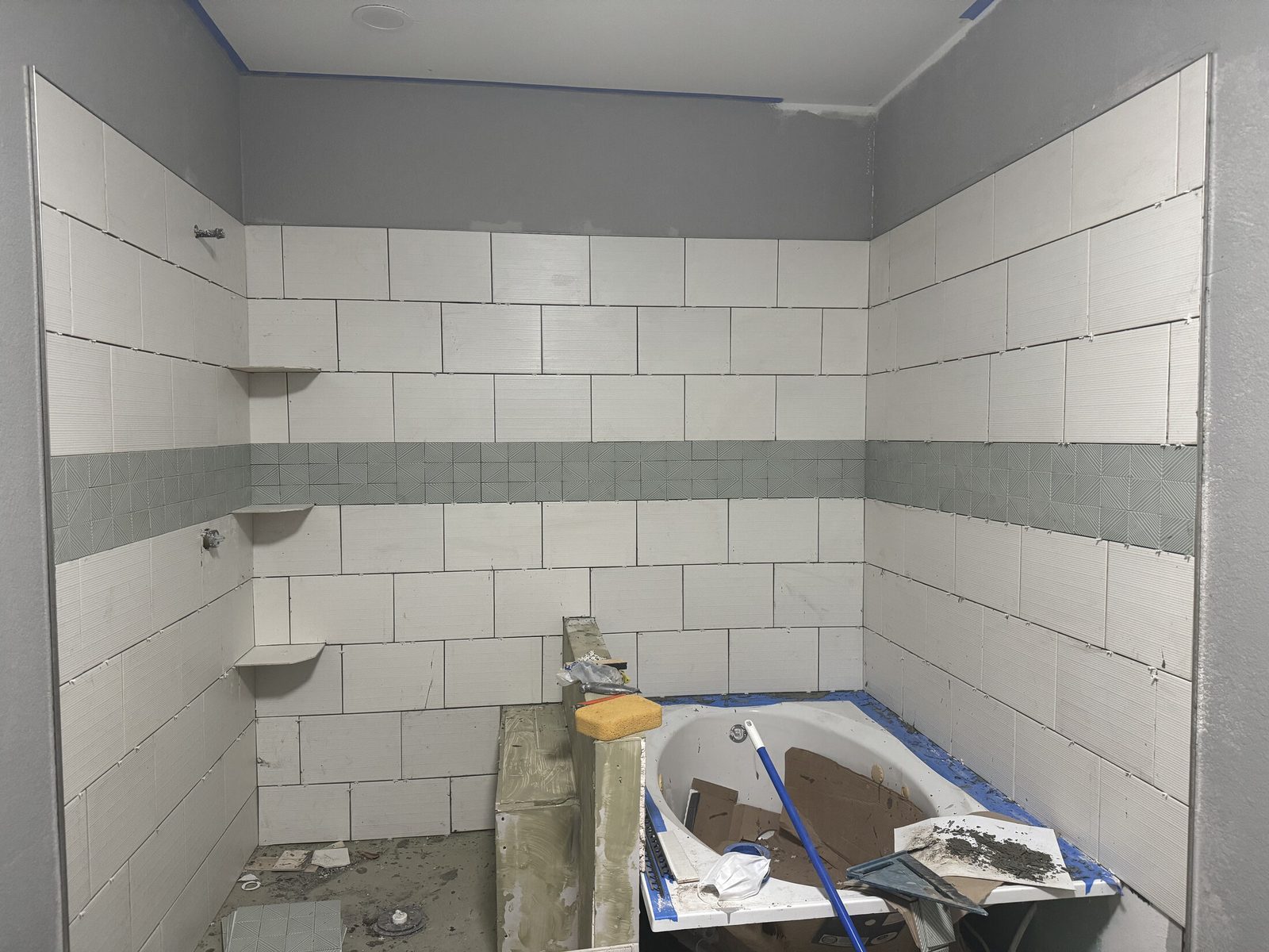 Ceramic subway tile shower and tub surround with a gray accent band and built-in corner shelves