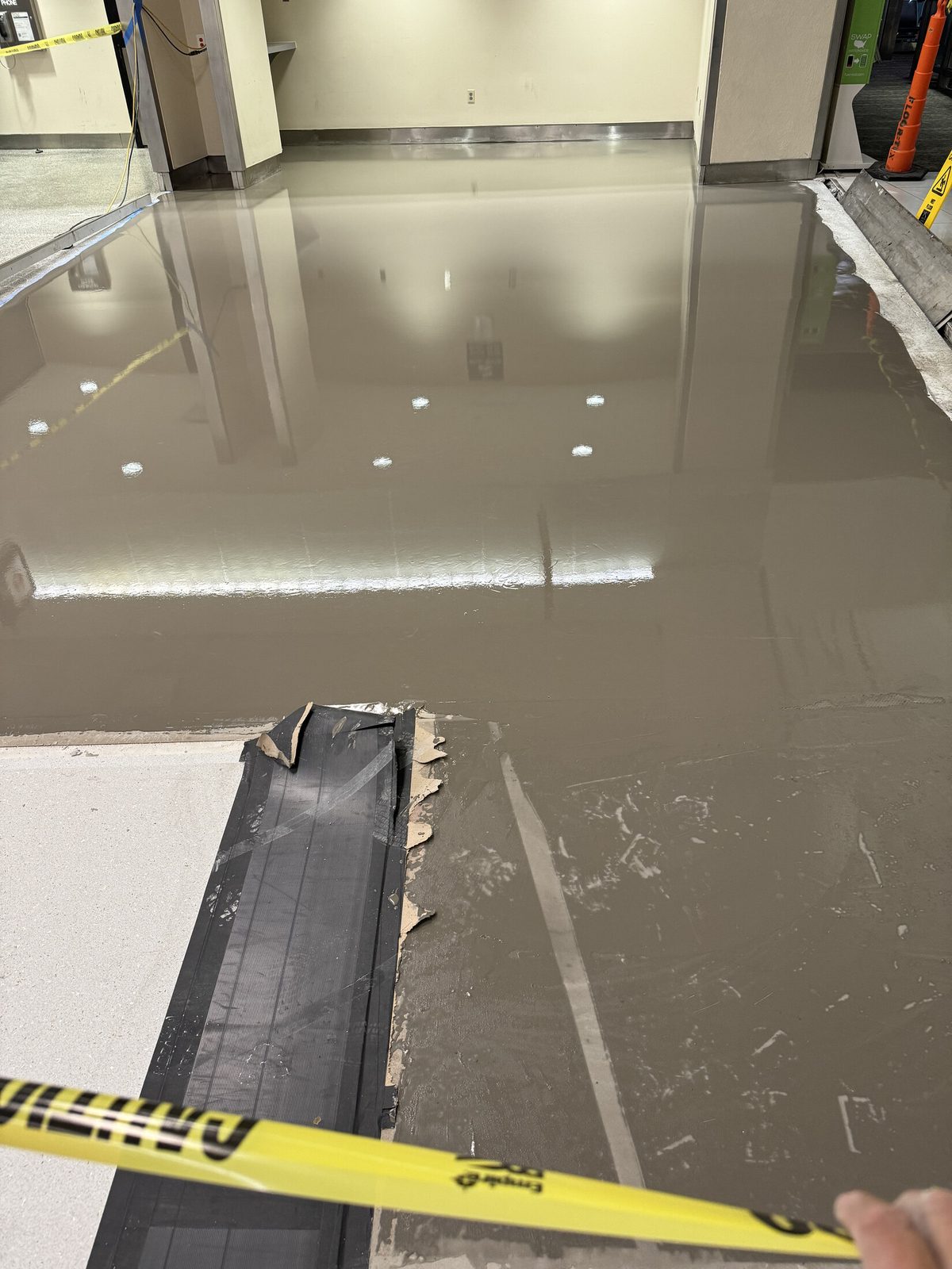 Self-leveling underlayment poured and flowing out flat across a commercial slab